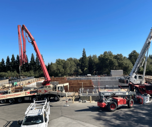 Two construction cranes lifting materials at a utility worksite.